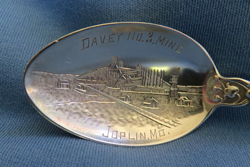 Souvenir Mining Spoon Bowl Davey No. 3 Mine Joplin MO.JPG - SOUVENIR MINING SPOON, TRI-STATE MINING DISTRICT DAVEY NO. 3 MINE JOPLIN MO - Sterling silver spoon, 5 5/8 in. long, engraved mining scene of mine buildings in bowl, handle open design at top, bowl marked DAVEY NO. 3 MINE, JOPLIN MO. reverse marked with maker’s mark and Sterling, ca.1910  [The Davey No. 3 mine is typical of hundreds of lead and zinc mines located throughout the nearly 2500 square miles of the Tri-State Mining District. The Tri-State district was a historic lead-zinc mining district located in southwest Missouri, southeast Kansas and northeast Oklahoma. The Davey mines were operated by the American Lead, Zinc and Smelting Company with general offices in Boston, MA.  The company was incorporated on January 26, 1899 in Maine and by 1919 owned 2,160 acres of mineral land in the Joplin district and leased another 655 acres of land owned by the Davey family which included four Davey mines.  As of 1919, two of the mines were producing and two others were worked out.  The Tri-State Mining District produced lead and zinc for over 100 years. Production began in the 1850s and 1860s in the Joplin - Granby area of Jasper and Newton counties of southwest Missouri. By the turn of the century Joplin with a population of 26,000 was quickly becoming the center of the mining activity for the Tri-State Mining District. The value of Tri-State mineral production from 1850 to 1950 exceeded one billion dollars.  Until 1945, the region was rated as the leading producer of lead and zinc concentrates in the world, accounting for one-half of the zinc and ten percent of the lead produced in the United States. Production continued until the closure of the Picher, Oklahoma mines in 1967, and the Swalley mine near Baxter Springs, Kansas in 1970. The Tri-State district includes three mining-related Superfund sites: the Tar Creek Superfund site in Oklahoma; the Jasper County and Newton County sites in Missouri; and the Cherokee County site in Kansas.]